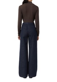 Braunes langärmliges Oberteil kombiniert mit weiten, dunklen Jeans mit hoher Taille und zwei Gesäßtaschen.
