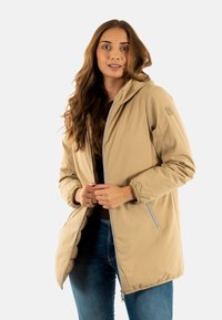Chaqueta con capucha beige con cierre de cremallera, puños elásticos y bolsillos laterales, hecha de un tejido suave y resistente al agua.