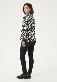 Zwart-witte geometrisch patroon lange mouwen shirt, aangesloten bij de taille, gecombineerd met zwarte skinny jeans en chunky zwarte schoenen.
