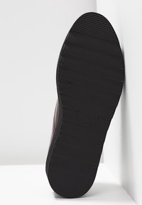 Semelle de chaussure en caoutchouc noir avec des rainures horizontales, arborant un logo de marque en relief. Le design est robuste et texturé pour une meilleure adhérence.