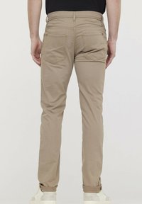 Pantalons en mélange de coton beige clair avec un design à jambe droite, comprenant deux poches arrière, des coutures subtiles et des ourlets retournés aux chevilles.