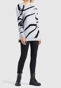 Felpa grigia con strisce zebrate nere a rilievo, scollatura a girocollo e maniche lunghe. Abbinata a jeans skinny neri e stivali militari neri.