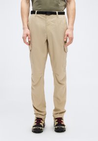 Μπεζ παντελόνια cargo από ελαφρύ ύφασμα, με πλαϊνές τσέπες, θηλιές για ζώνη και άνετη εφαρμογή. Συνδυασμένα με μαύρα και κόκκινα ορειβατικά μποτάκια.