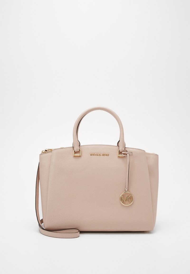 Sac à main beige Michael Kors avec double poignées, bandoulière amovible, pendentif logo doré et fermeture éclair sur le dessus.