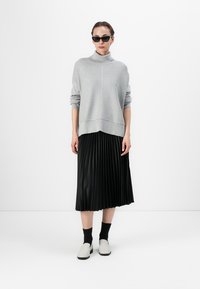 Lys grå turtleneck genser, svart plisserte midiskjørt, hvite slip-on sko og solbriller. Glatt tekstur, avslappet passform og lagdelt look.