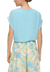 Blouse bleu clair à manches courtes en tissu lisse, associée à une jupe à motifs avec des designs cachemire dans des couleurs pastel.