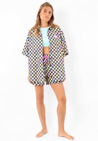 Ensemble de chemise à carreaux et de shorts dans des couleurs pastel. Le tissu est léger et la coupe est ample. La chemise a des manches courtes et un col ; les shorts possèdent un cordon de serrage.