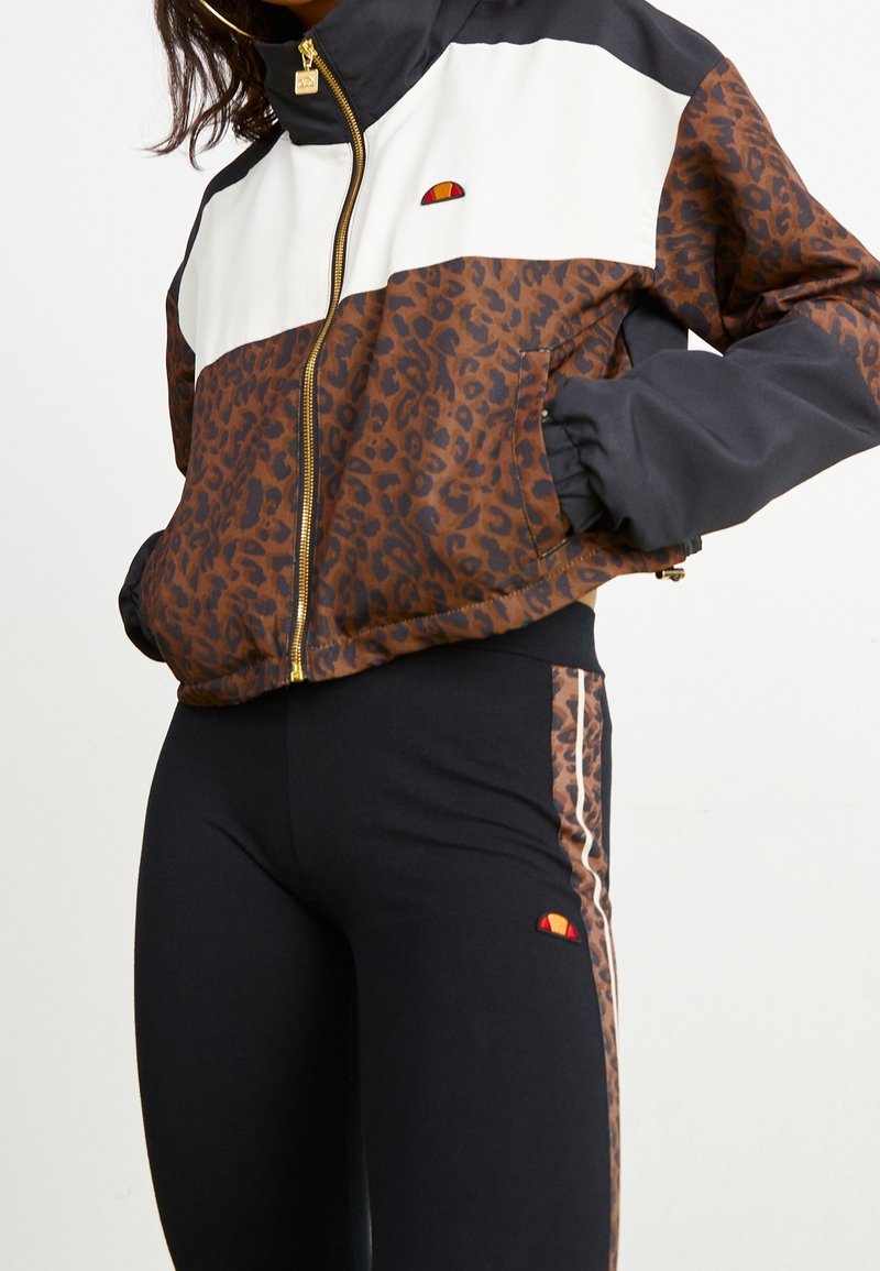 Leopardmönstrad zip-up jacka i brunt med svarta ärmar och vit bröstpanel. Svarta leggings med leopardrand. Accentuerad med logotyper.