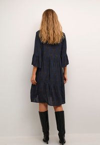 Vestido azul marino con estampado floral, diseño con volantes, mangas con volantes y textura suave. Combinado con botas negras hasta la rodilla.