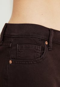 Jeans din denim maro, cu un mic buzunar posterior și accesorii de culoare cupru. Țesătura are o textură de twill și un design clasic.