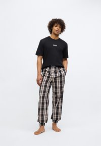 Tricou negru cu mânecă scurtă, cu logo-ul "BOSS", asortat cu pantaloni de pijama în carouri, în nuanțe de negru, bej și maro, având manșete elastice și o croială lejeră.