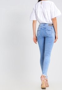 Jeans skinny azzurri chiari con orlo sfilacciato, due tasche posteriori con dettagli di cucitura, indossati con un top bianco e tacchi beige.