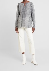 Czarna i biała bluzka w długim rękawie z dekoltem typu keyhole, zestawiona z białymi, szerokimi spodniami oraz białymi botkami na słupku.