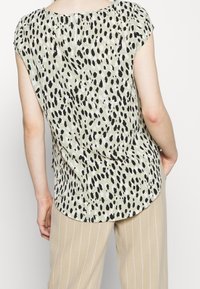 Blusa verde chiaro con stampa a pois bianco e nero, maniche corte e chiusura con zip sul retro; tessuto liscio.