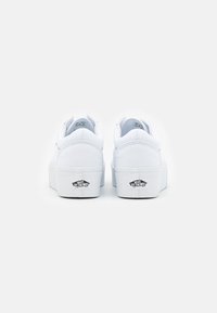 White canvas sneakers with a thick sole, featuring a smooth texture, round toe, and a contrasting black logo on the heel.