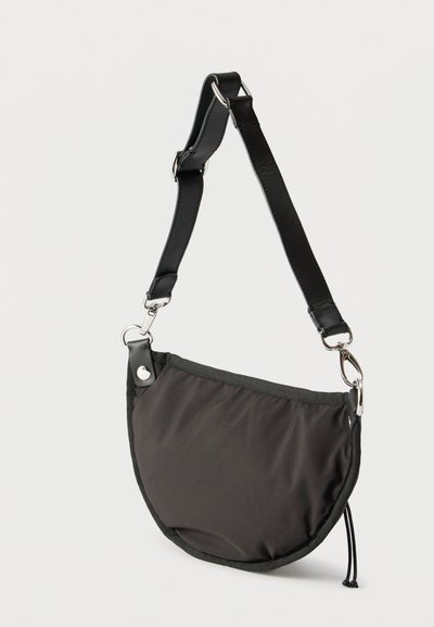 Μαύρο τσάντα ώμου σε σχήμα μισοφέγγαρου με ρυθμιζόμενο δερμάτινο λουράκι και ασημένια εξαρτήματα σε απλό ανοιχτό φόντο.