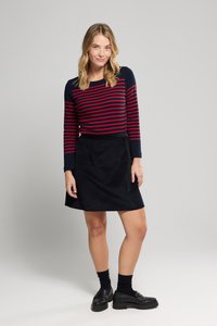 Rød og marineblå stribet langærmet top parret med en sort ruskindsnederdel. Sorte sko og sokker fuldender outfittet. Simpelt design og tekstur.