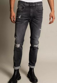 Vybledlé černé džíny s odřenými detaily, slim fit, pět kapes, ohrnuté nohavice, spárované s černými koženými botami.