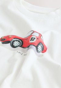 Červené kreslené závodní auto s číslem 82 a nápisem „Race Day“ na bílé látce, detailní záběr límce mikiny a potisku.