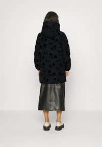 Chaqueta acolchada negra con patrón en relieve de Mickey Mouse, fabricada con tejido impermeable, con capucha y puños acanalados, combinada con una falda de cuero negra y zapatos beige.