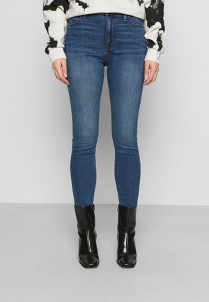Jeans de mezclilla azul ajustados con una textura suave y un desvanecimiento mínimo, combinados con elegante botas de tobillo negras con puntera afilada.