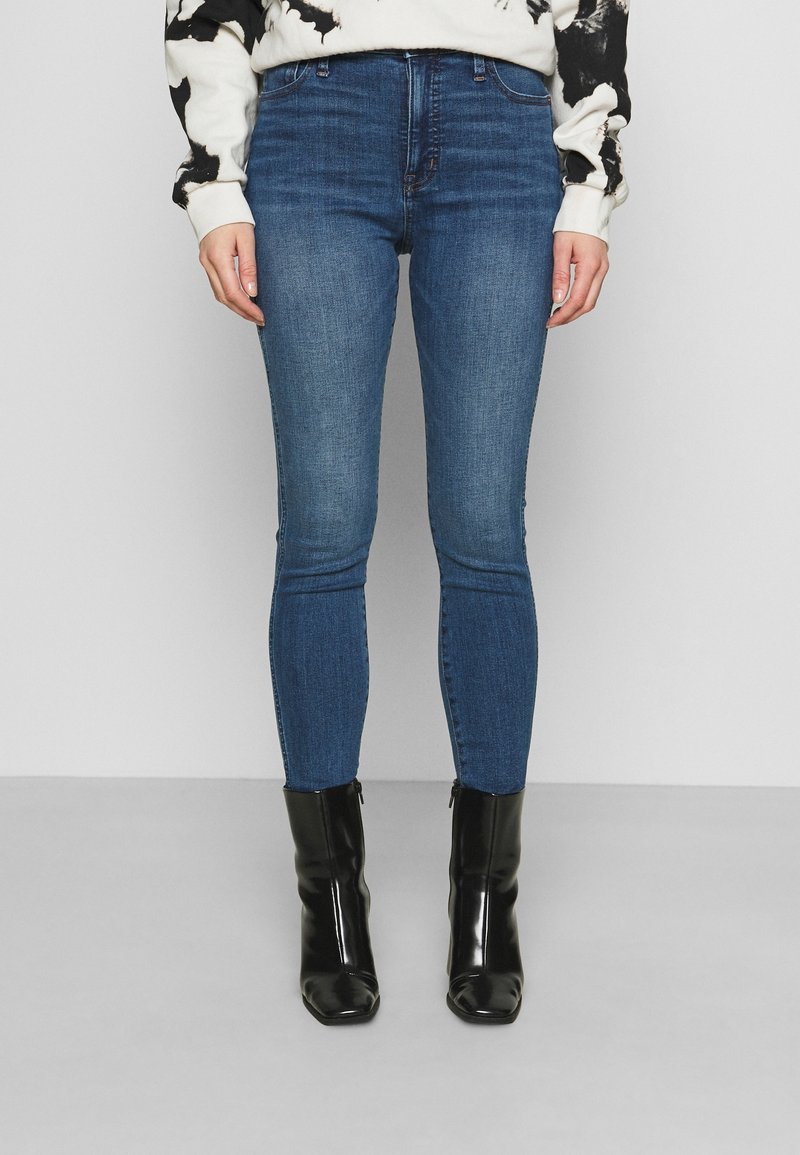 Tunna blå denimjeans med en slät textur och minimalt blekning, i kombination med svarta eleganta ankelstövlar med spetsig tå.