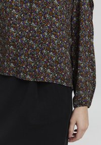 Blomstrete topp med svart bakgrunn, prydet med små oransje, lilla og hvite blomster. Langermet med elastiske mansjetter og avrundet kant.