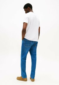 Camiseta blanca de manga corta, jeans azules y zapatos de slip on color beige. Los jeans tienen bolsillos traseros y un corte recto. Vista trasera del conjunto.