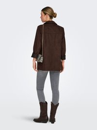 Brown suede jacket with a collar, rolled sleeves, paired with gray skinny jeans and black cowboy boots. Small patterned crossbody bag.