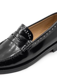 Mocassini in pelle nera con finitura lucida, cuciture decorative e borchie metalliche lungo il lato. Suola piatta con leggero tacco.
