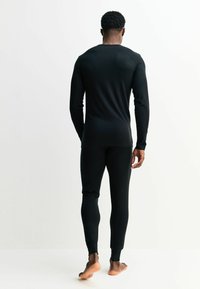 Fekete hosszú ujjú termikus felső és hozzá illő nadrág, testhezálló kialakítás, puha anyag, minimális varrási részletek, és bordázott szegélyek az ujjakon és bokákon.