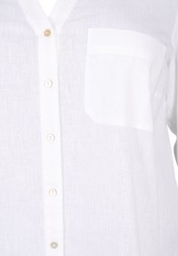 Camicia di lino bianca con chiusura a bottoni, taschino sul lato sinistro del petto e una finitura morbida e strutturata. I bottoni sono di colore chiaro.