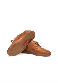 Chaussures en cuir tan avec un bout rond, un design à lacets et une semelle en caoutchouc texturée. Présente un petit logo rouge sur le côté de la semelle.