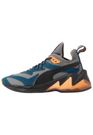 La sneaker présente une tige en mesh gris, bleu et noir avec des accents orange. Semelle épaisse avec un design en zigzag distinctif. Fermeture à lacets.