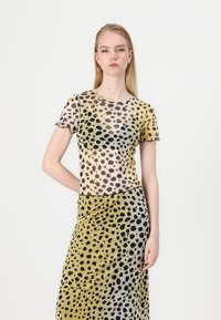 Top giallo trasparente con motivo a pois neri, maniche corte, scollatura rotonda e bordi arricciati, abbinato a una gonna a pois coordinata.