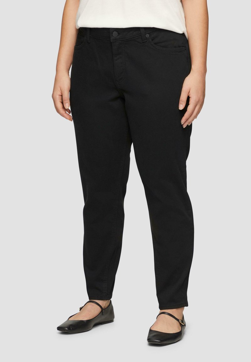 Pantalons en mélange de coton noir avec une coupe droite, design à cinq poches et fermeture à bouton sur le devant, associés à des chaussures plates noires.