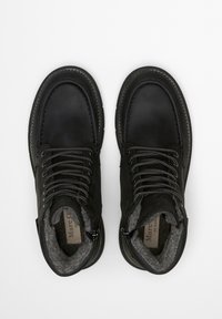 Schwarze Lederstiefel mit grauem Fleecefutter, ausgestattet mit runden Schnürsenkeln, robusten Ösen und kontrastierenden Nähten. Rundspitz-Design.