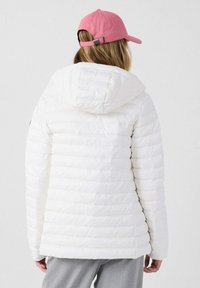 Giacca a vento trapuntata bianca con cappuccio, caratterizzata da cuciture orizzontali e una vestibilità leggermente comoda. Abbinata a un berretto rosa.