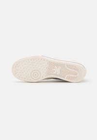 White sneaker sole with a textured rubber tread. Features circular and zigzag patterns, smooth edges, and a flat profile.