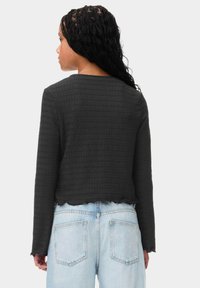 Zwarte textuurjas met een cropped ontwerp en een geschulpte zoom, gecombineerd met lichtblauwe high-waisted jeans. Details zijn onder andere lange mouwen.