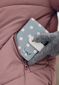Light blue wallet with pink polka dots, white clasp, and silver logo, partially visible in a pink puffer jacket pocket. Gray, textured glove nearby.