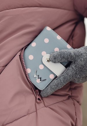 Light blue wallet with pink polka dots, white clasp, and silver logo, partially visible in a pink puffer jacket pocket. Gray, textured glove nearby.