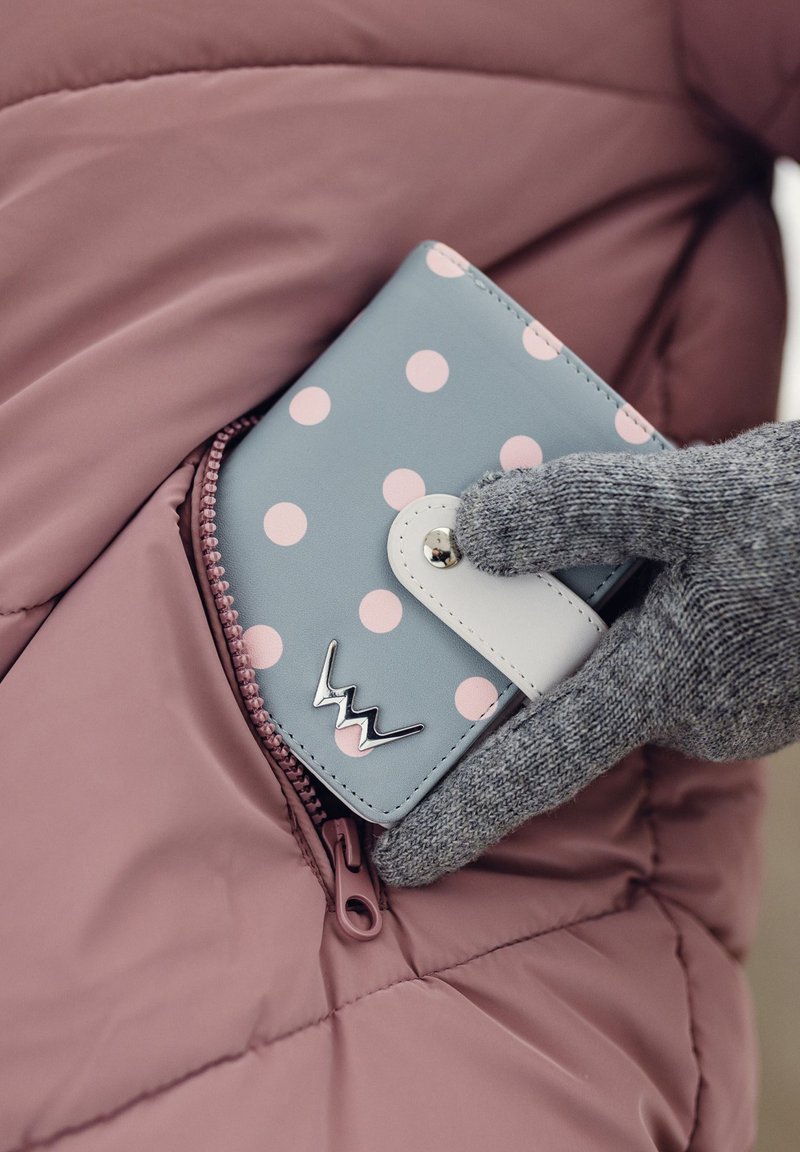Light blue wallet with pink polka dots, white clasp, and silver logo, partially visible in a pink puffer jacket pocket. Gray, textured glove nearby.