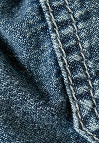 Närbild av blå denimtyg som visar detaljerad vävtextur och dubbel vit söm.