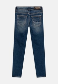 Tmavě modré džíny s úzkým střihem, obsahující dvě zadní kapsy a jemné vyblednutí. Pás má viditelnou značkovou etiketu.