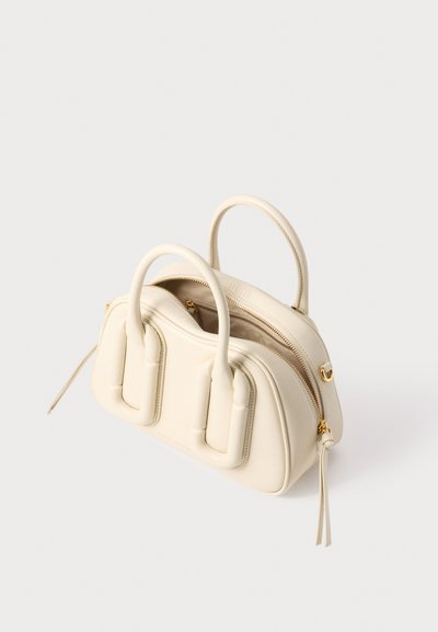 Sac à main en cuir couleur crème avec deux poignées arrondies, un compartiment principal zippé avec fermeture éclair dorée et des détails matelassés sur le panneau avant.