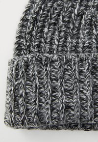 Berretto lavorato a maglia grigio con un design a coste testurizzato; presenta filamenti di lana bianca e grigia scura intrecciati insieme. Materiale spesso e caldo.
