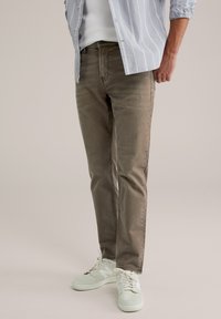 Svijetlosiva prugasta košulja preko prilagođene bijele majice, uparena s maslinasto zelenim trapericama i bijelim tenisicama. Glatka tkanina, ležeran dizajn.