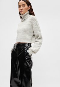 Camisola de gola alta cinza clara em malha com design cropped e textura canelada, combinada com calças pretas brilhantes de cintura subida.