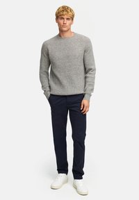 Grau gerippter Strickpullover mit einem runden Halsausschnitt, kombiniert mit navyfarbenen Hosen und weißen Sneakers. Einfaches, strukturiertes Design und weiche Textur.